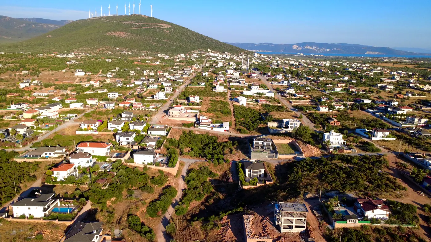 Aerial panorama of Yeşiltepe, Didim — established street grid, villas and wind turbines on the hilltop